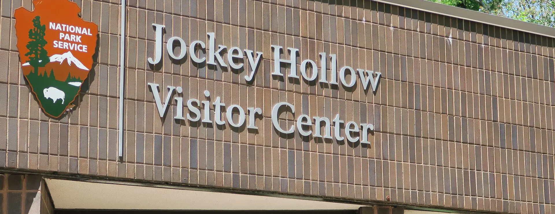 Entrance sign for the Jockey Hollow Visitor Center featuring the National Park Service arrowhead logo on a brown tiled wall.