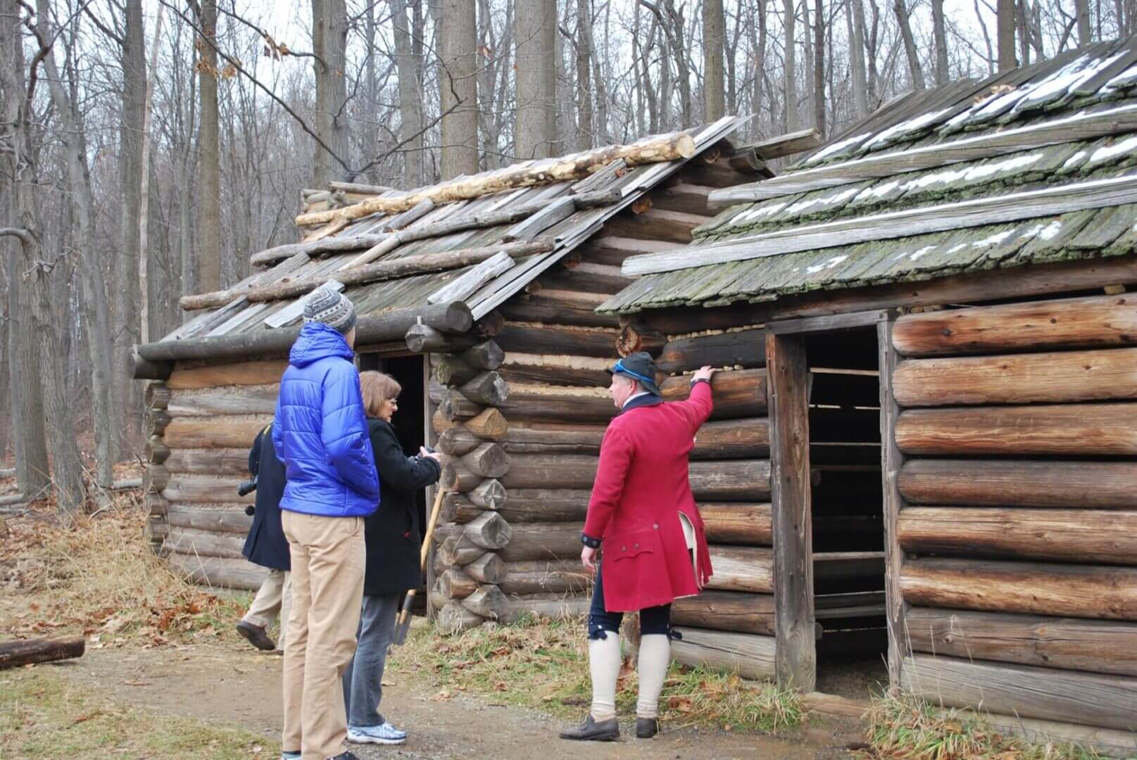 People visiting historical log cabins in forest.
